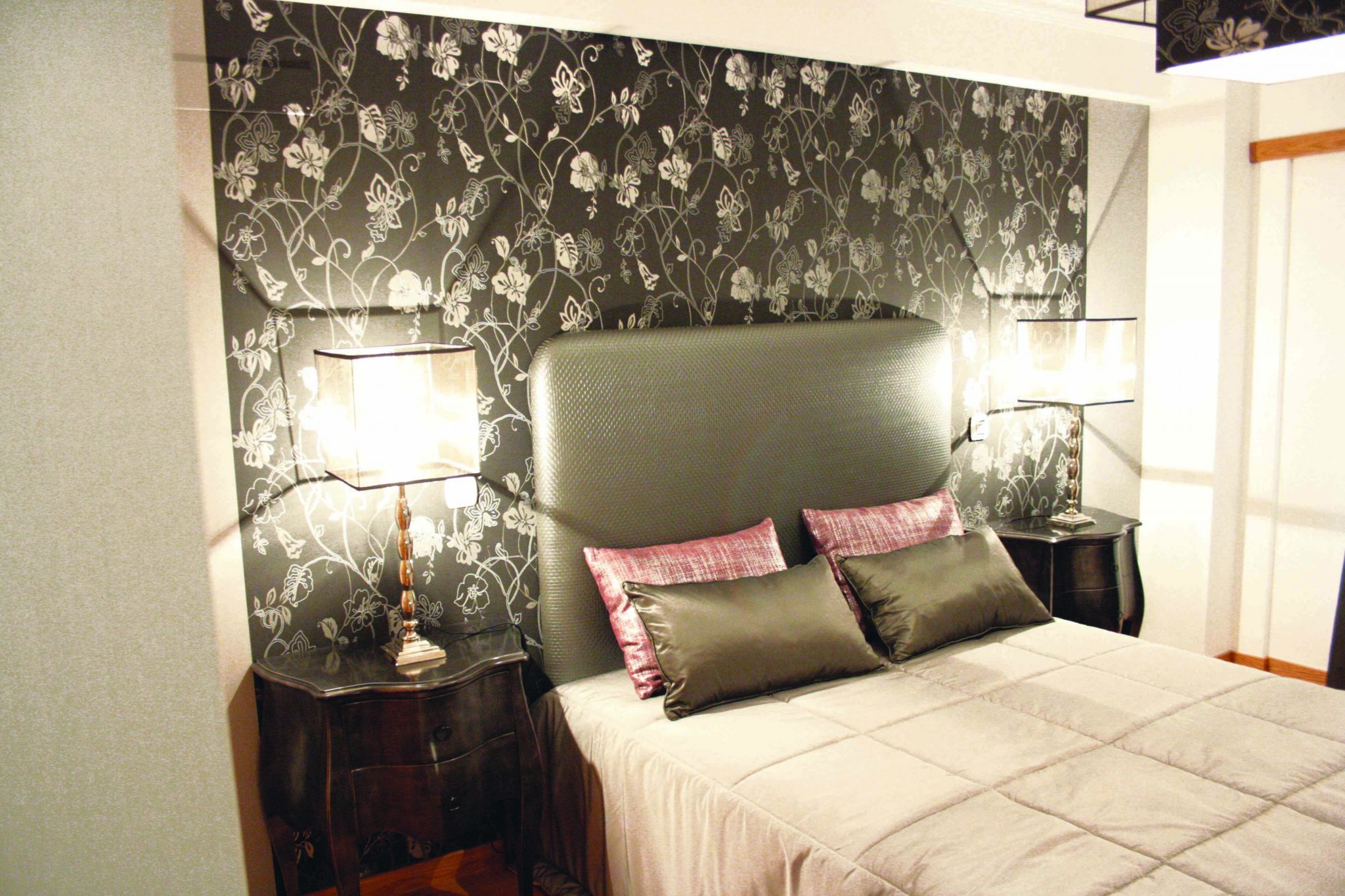 Quarto de casal com papel de parede floral e cabeceira estofada por medida